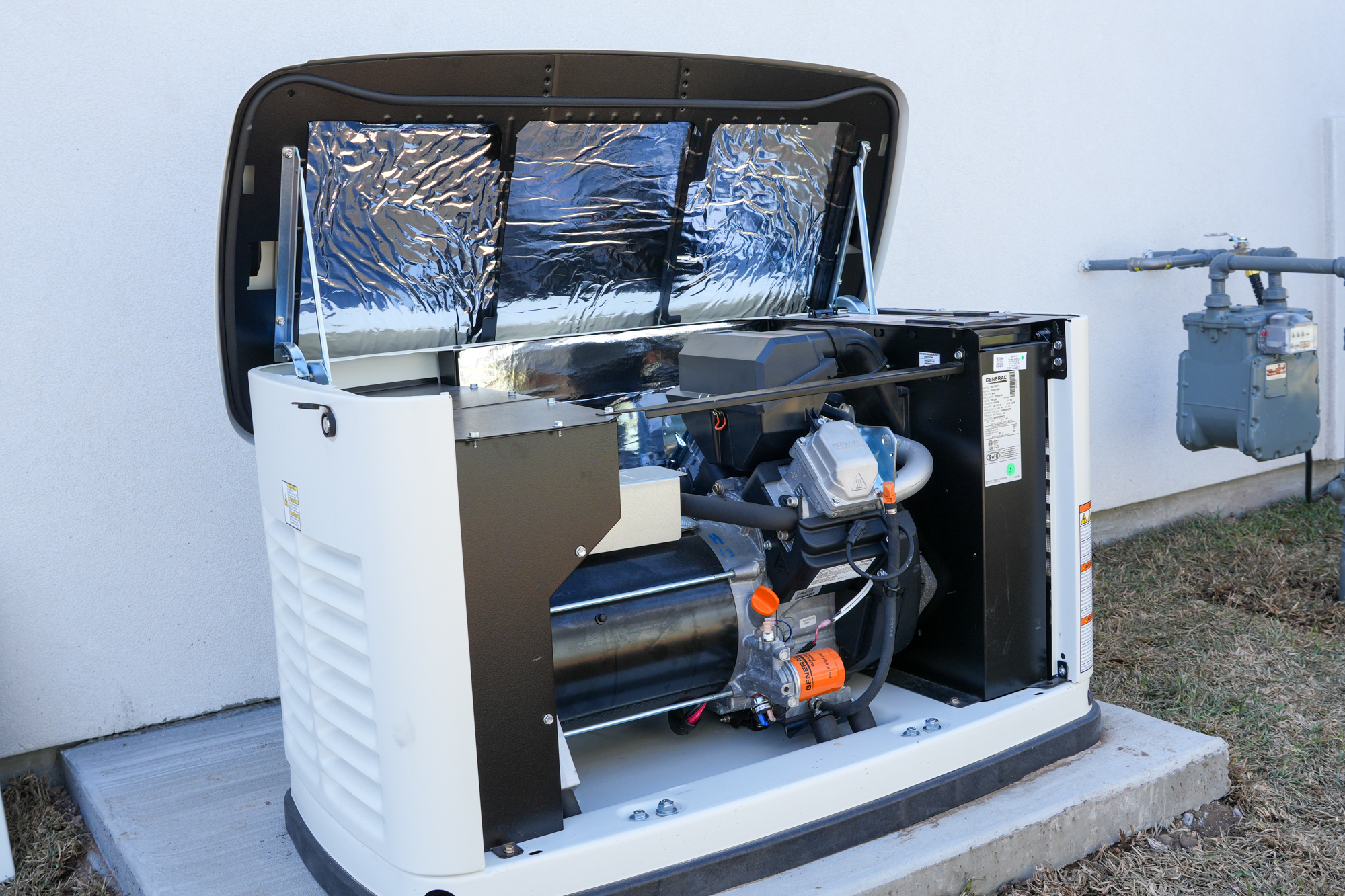 Open home standby generator installed beside a wall with gas meter nearby