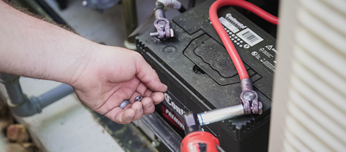 Technician testing a home standby generator battery with a multimeter.